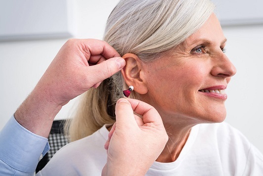 Ältere Frau bekommt ein modernes Hörgerät vom Akustiker ins Ohr eingesetzt.